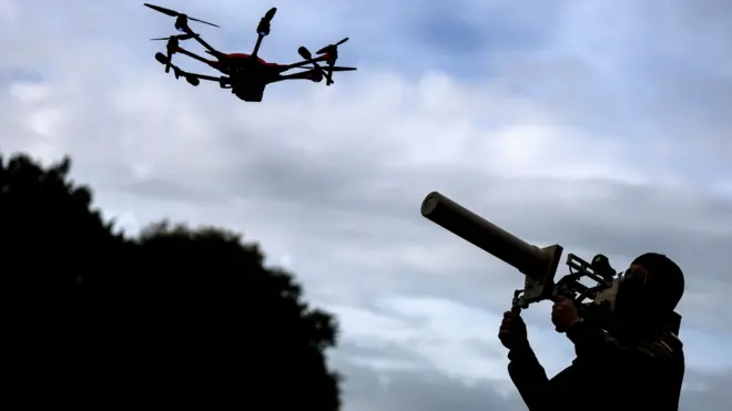 Солдат направляет устройство для подавления дронов на дрон в небе.