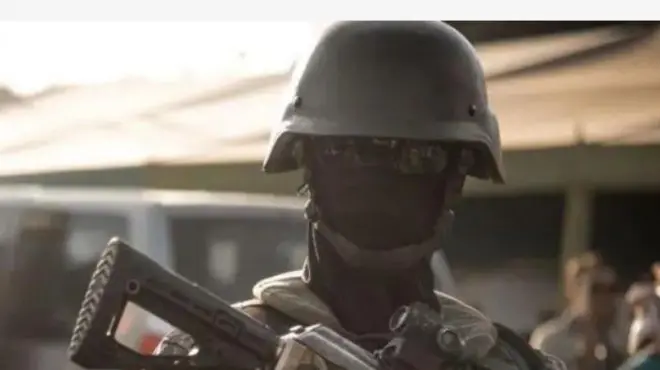 Aworan ọkunrin to wọṣọ ologun to si dihamọra, o gbe ibọn dani, bo oju rẹ.