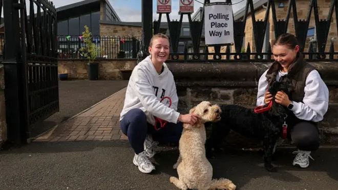 若い女性が2人、投票所の前で犬と一緒にいる