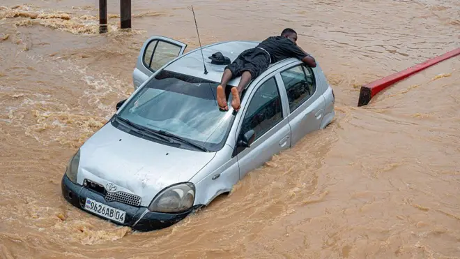 Ifoto ifatiwe hejuru igaragaza umugabo uryamye hejuru y'imodoka kugira ngo amazi y'imyuzure atamutwara, nyuma yuko amazi yuzuye mu muhanda kubera imvura nyinshi yaguye mu karere ka N'djili k'i Kinshasa. Ifoto yo ku itariki ya 6 Mata (4) mu mwaka wa 2025.