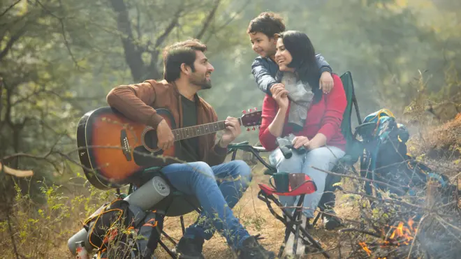 তরুণ একজন পুরুষ গিটার হাতে একটি চেয়ারে বসে আছেন, তার সামনে একজন নারীও আরেকটি চেয়ারে বসা, তার পেছনে একটি শিশু হাত দিয়ে ওই নারীর কাঁধ জড়িয়ে আছে। সবার মুখে হাসি। তারা একটি বনের মাঝে বসে আছেন। তাদের সামনে কয়েকটি লাগড়িতে আগুন জ্বলছে