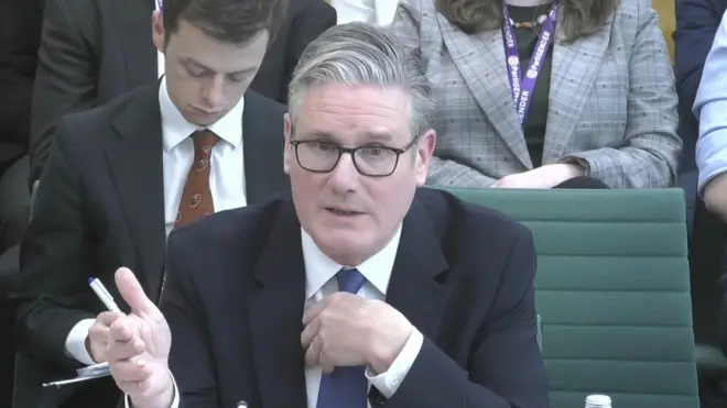 スーツにめがね姿のスターマー首相が、机に座って話している。背後には傍聴している人たちが並んで座っているのが見える