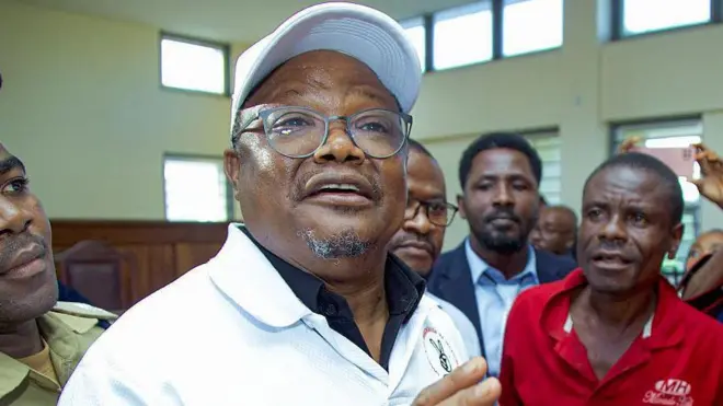 Tundu Lissu yambaye ingofero y'umweru n'umupira ufite ikora, avugana n'abamushyigikiye, aha ni ku rukiko i Dar es Salaam, muri Tanzania. 