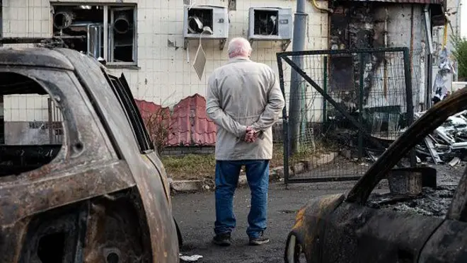 старий чоловік дивиться на зруйнований будинок