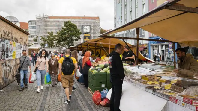 المتسوقون في سوق هيرمانبلاتز اليومي بالقرب من شارع سوننآليه في برلين، ألمانيا، يوم الاثنين، 13 سبتمبر 2021. غيّر اللاجئون السوريون الطابع الثقافي لعاصمة ألمانيا بطريقة لم تشهدها البلاد منذ الستينيات، حيث يُعرف شارع سوننآليه محلياً باسم "الشارع العربي"، وقد يكون أقرب شيء للوطن بالنسبة للعديد من السوريين.