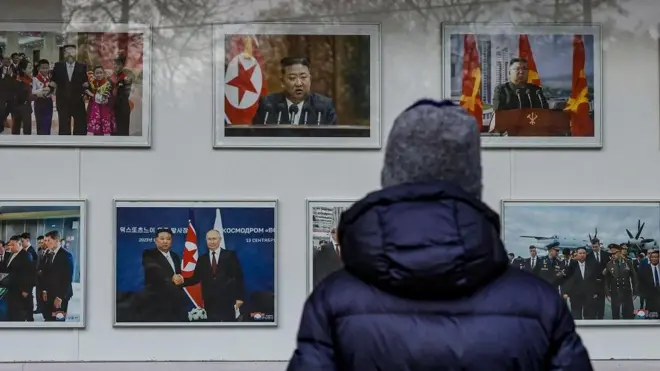 一名身穿藍色羽絨外套、頭戴灰色帽子的男子透過窗戶觀看朝鮮領導人金正恩的照片。