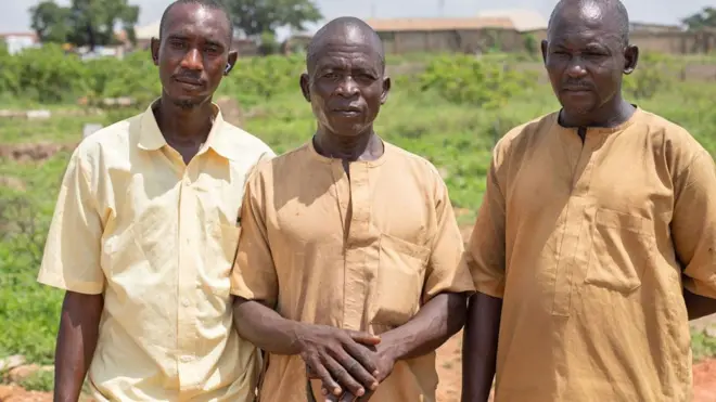 Magaji Abdullahi (C), les mains posées sur le manche d'une bêche, debout entre ses cousins et ses deux cousins Aliyu (G) et Abdullahi (D) au cimetière de Tudun Wada, dans l'État de Kaduna, au Nigeria.