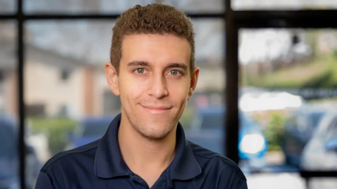 Молодой человек с короткими волосами и зеленоватыми глазами улыбается, глядя в кадр