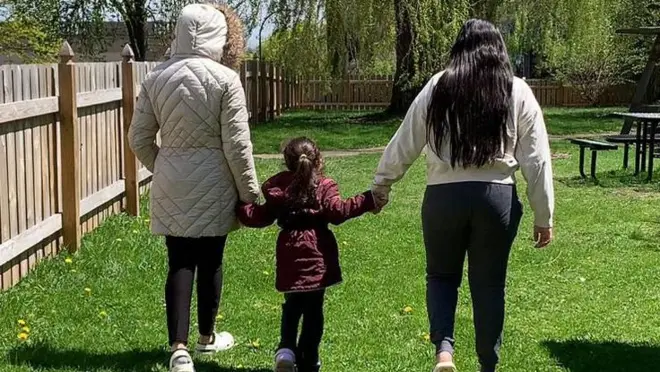 Aracely de espaladas con sus dos hijas en un refugio en Buffalo, NY.