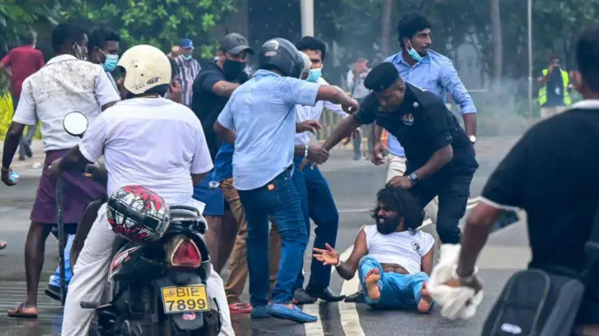 2022 මැයි 9 වන දින කොළඹ ජනාධිපති කාර්යාලයෙන් පිටත විරෝධතාකරුවන් සහ රජයේ ආධාරකරුවන් ගැටෙන අතරතුර, පොලිස් නිලධාරියෙකු බිම වැටී සිටින පුද්ගලයෙකුගේ හිසකෙස්වලින් අල්ලාගෙන සිටියි.