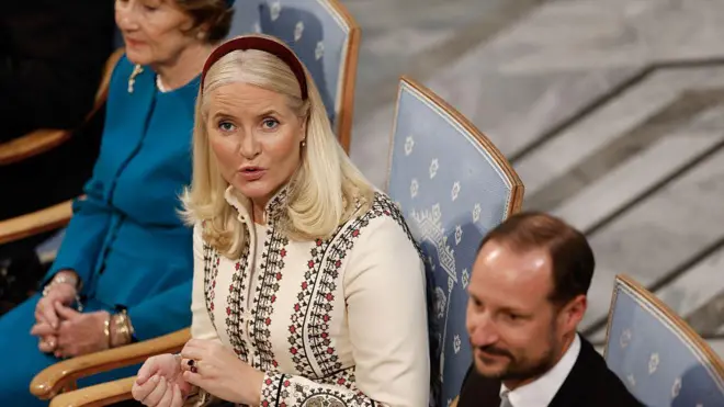 Norveç Veliaht Prensesi Mette-Marit bir sandalyede oturmuş. Yukarıdan çekilmiş fotoğrafta prenses yukarı doğru bakıyor. Yanında Veliaht Prensi Haakon var. 