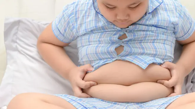 un niño con sobrepeso sosteniéndose el abdomen