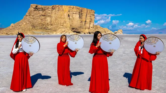 Cuatro mujeres iraníes con vestidos rojos y sosteniendo imágenes circulares realizan una actuación en el lecho seco del lago Urmia el 11 de abril de 2023, para llamar la atención sobre las crisis del cambio climático.