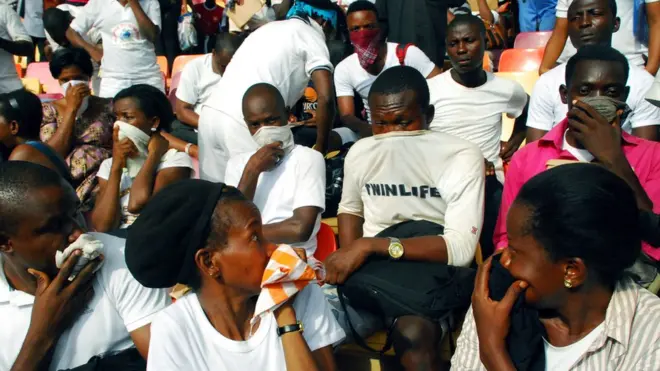 Job-seekers cover their nose and mouth for safety after security agents from the immigration services threw a cannister of tear gas to disperse the crowd in Abuja