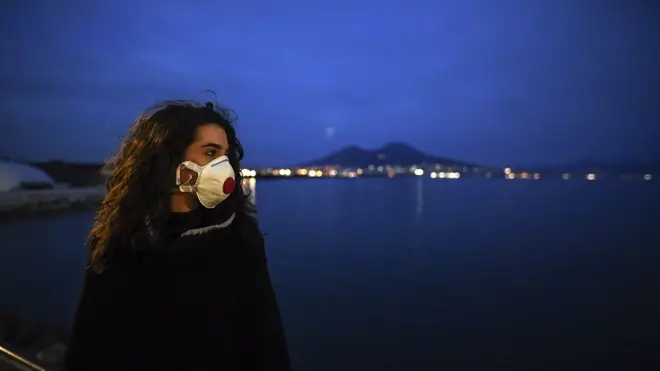 A woman wearing antivirus masks, to protect herself from the Coronavirus (Covid 19) waiting for a super moon walks at sunset on the Naples waterfront in front of the Vesuvius volcano.