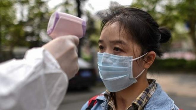 A man wearing a protective suit checks a woman's temperature next to a residential area in Wuhan, in China"s central Hubei province on April 7, 2020.