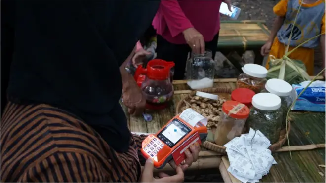 Seorang pedagang Pasar Semarangan Tinjomoyo melayani pembeli dengan mesin uang elektronik.