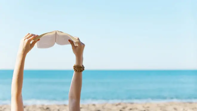 Una mujer lee un libro en la playa.