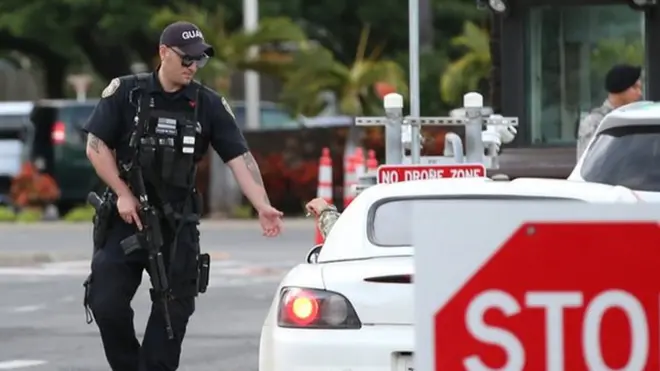 A guard armed with an assault rifle checks vehicles entering the Nimitz Gate entrance of Joint Base Pearl Harbor Hickam