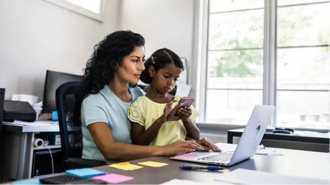 Una mujer trabaja en la computadora junto a una niña.
