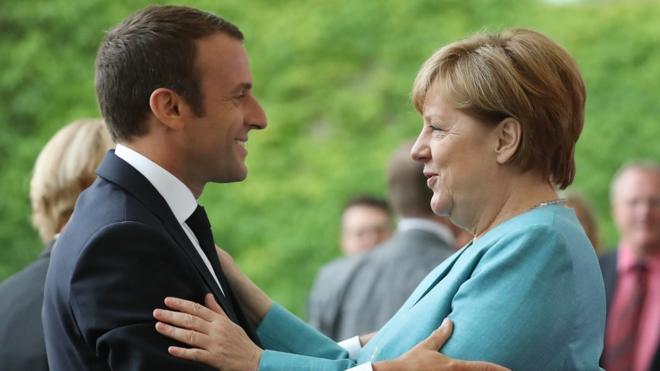 Emmanuel Macron, left, in his dark suit, hugs Angela Merkel, right, in a light blue jacket, at the June 2017 G7 Summit