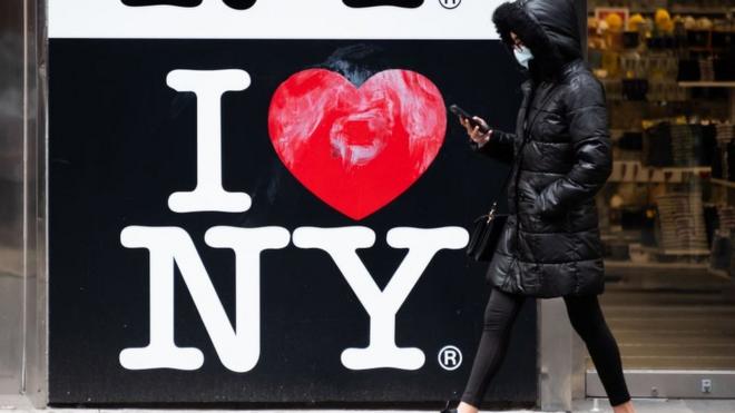 Una mujer pasando por una señal de "I love New York"
