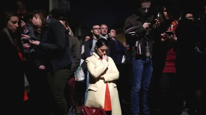 Seorang perempuan berlutut selagi Katedral Notre-Dame dilalap api.