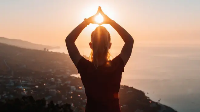 Un mujer en práctica de mindfulness con el Sol de fondo.