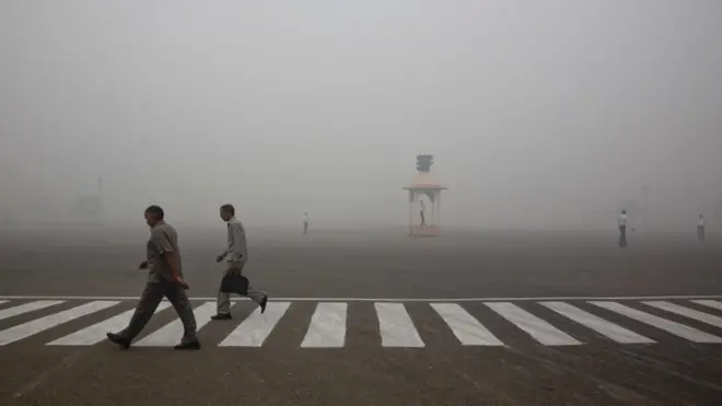 Indians walk to work as Delhi traffic police officers manage an intersection enveloped by smoke and smog, on the morning following Diwali festival in New Delhi, India, Monday, Oct. 31, 2016.