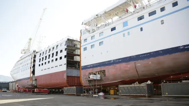 La sección central se fabrica en un lado mientras los operarios seccionan el barco por la mitad.