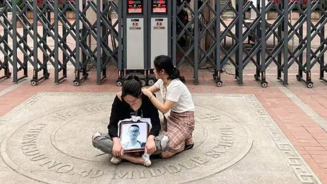 林唯麒的母親魯女士抱著孩子的相片坐在學校門前。