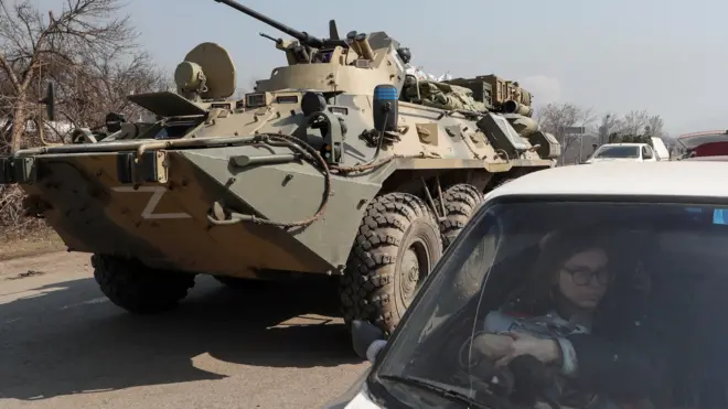 A refugee waits in a car as an armoured personnel carrier of pro-Russian troops drives out of a checkpoint in the besieged city of Mariupol