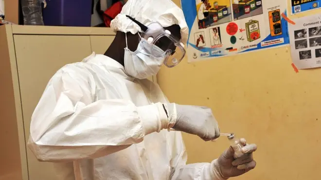 Health worker wey hold injection.