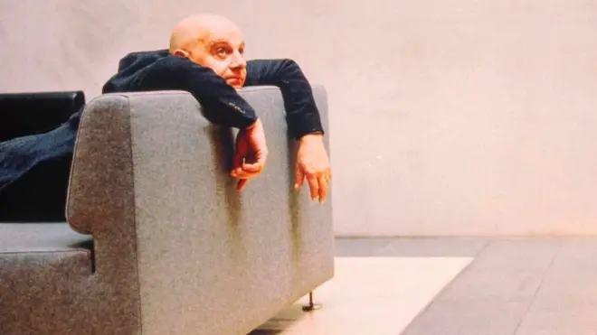 Una persona vestida formalmente, pero recostada contra el respaldo de un sofá