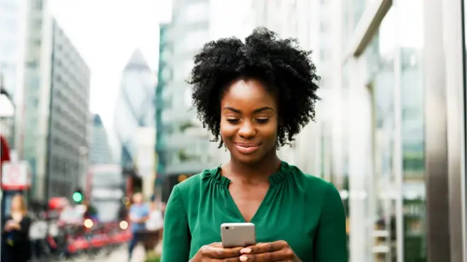 Une femme noire qui regarde son téléphone dans la rue