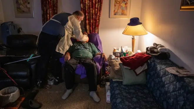 Un ambulancier portant un équipement de protection individuelle (EPI), met un masque chirurgical à un patient afro-américain présentant les symptômes du COVID-19 dans son appartement.