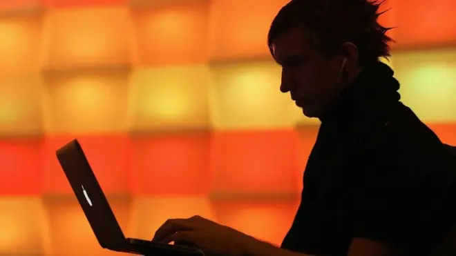 Un hombre a contraluz, trabajando en una laptop