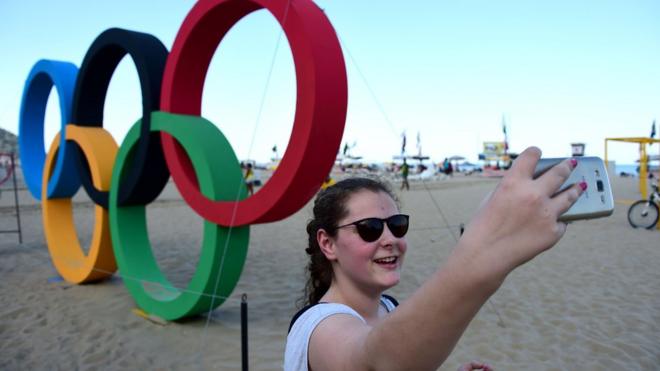Woman taking selfie in front of Olympic rings on Copacabana Beach - August 1, 2016.