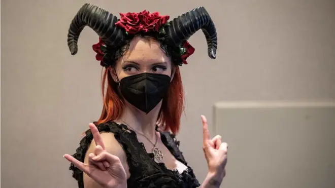 A woman poses for photos giving the sign of the horns at SatanCon in Boston, Massachusetts