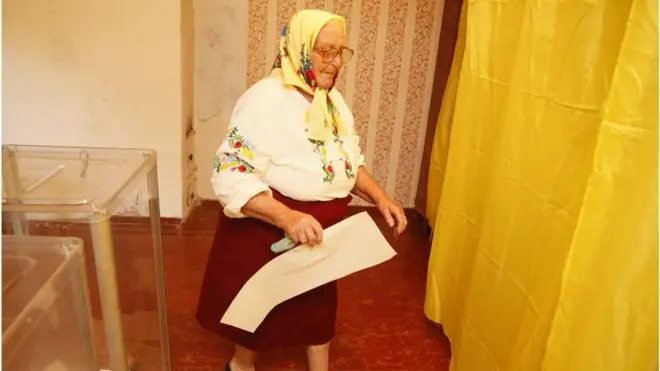 Літня жінка заходить в кабіну для голосування