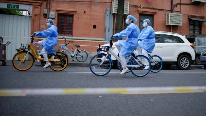 一群身穿全身防护衣的防疫人员在上海街头骑乘共享自行车（15/4/2022）
