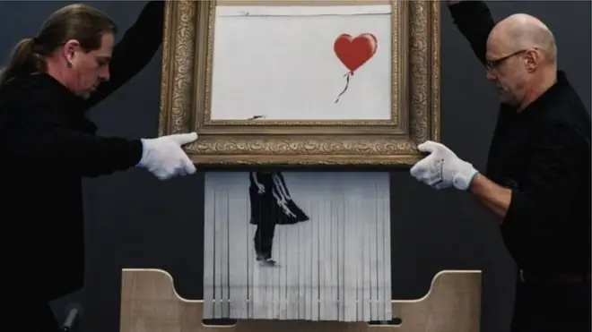 Служители музея держат картину Бэнкси