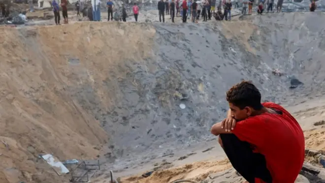 Momak čuči pored kratera od izraelske bombe u gazi