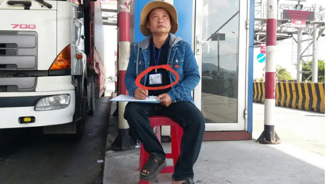 Ông Nguyễn Minh Hùng đeo chứng minh thư ngồi đếm xe qua trạm BOT Ninh Lộc