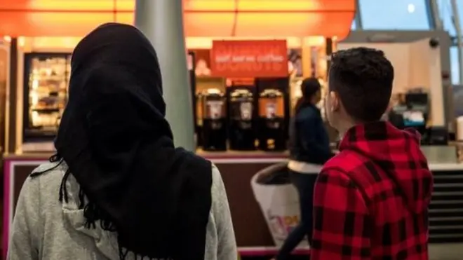 A young woman in a Hijab watches the arrivals board at New York's JFK airport