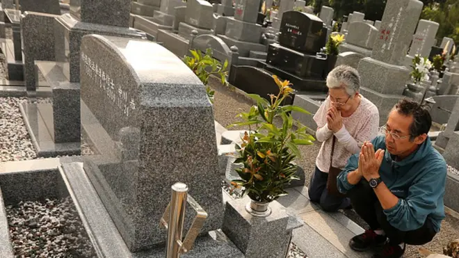 Um homem e uma mulher rezando na frentecomo sempre ganhar na roletaum túmulo no Japão