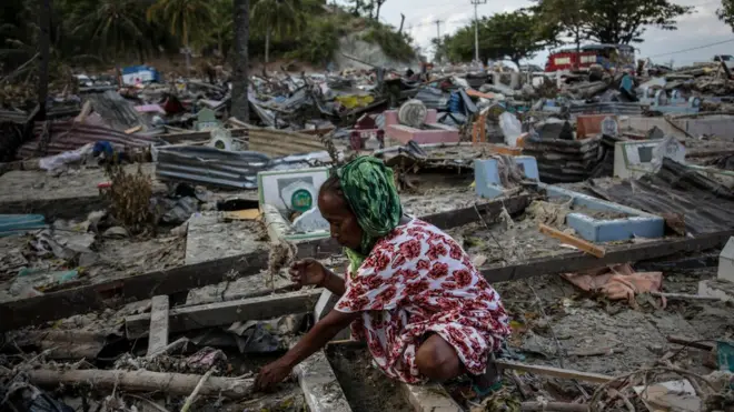 Seorang perempuan membersihkan makam orang tuanya yang tertimbun material bangunan akibat gempa-tsunami yang menerjang Sulawesi Tengah.