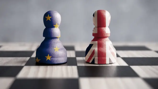 Two chess pieces on a chess board, one enclosed in the EU flag, one enclosed in the union jack.
