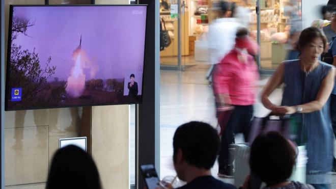 Passengers wait at a train station in front of a TV news report on North Korea firing a ballistic missile off its east coast on July 12