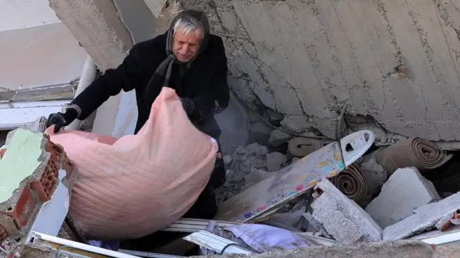 A man gathers a blanket under a collapsed building in Kahramanmaras, Turkey